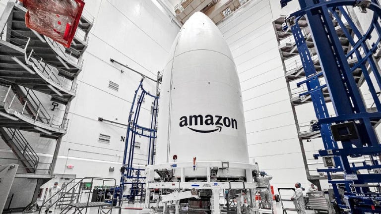 A giant rocket logo featuring a giant Amazon logo with a smiley arrow, intended to house the Atlas V rocket, sits on a hanger before launch.