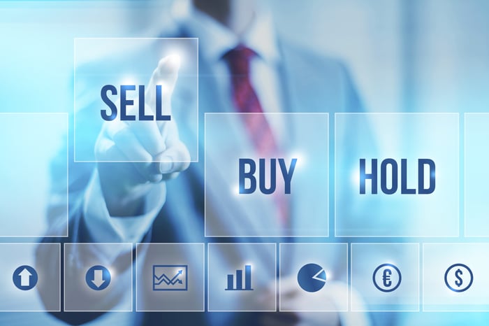 A trader presses the sell button on a large digital screen.